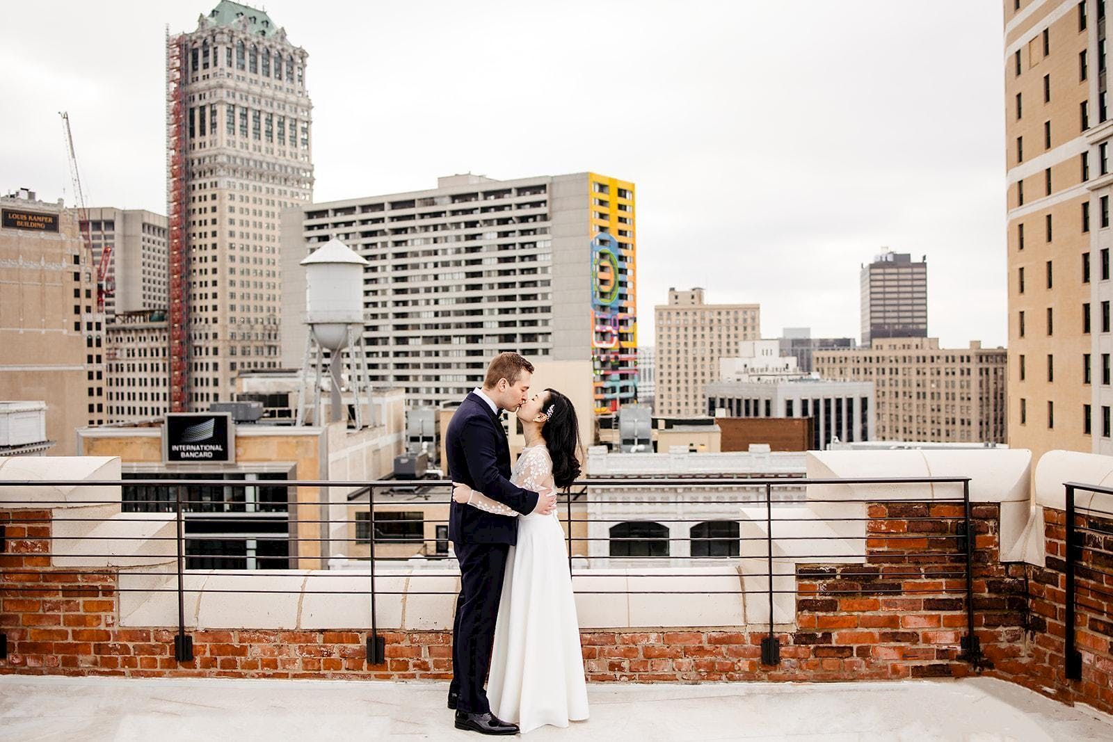 A couple is embracing on a rooftop with an urban skyline backdrop of tall buildings.