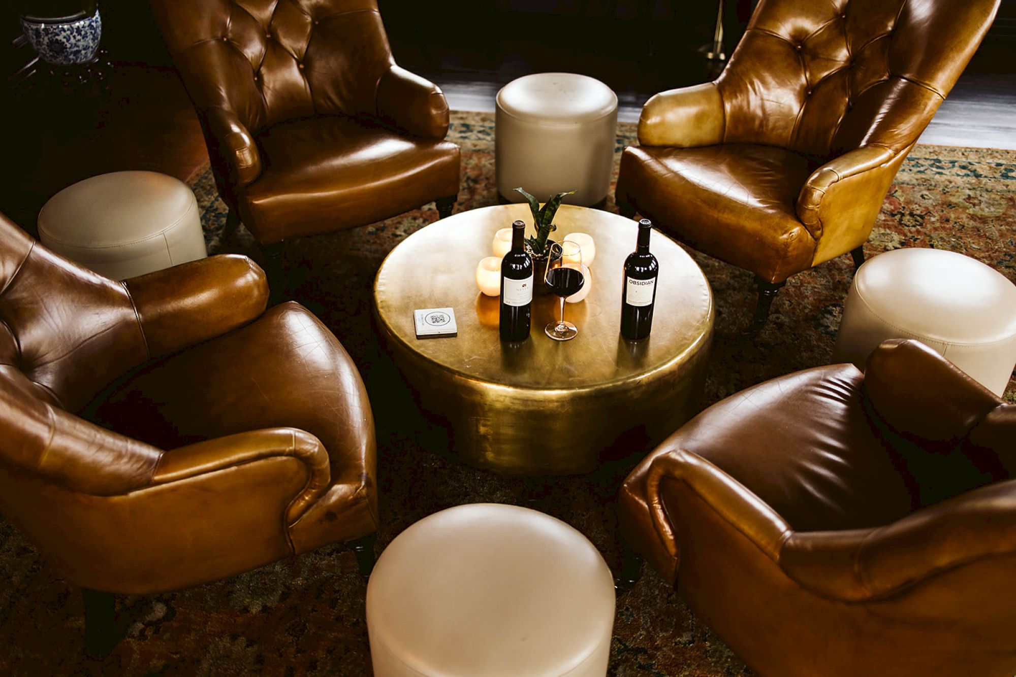 A cozy seating area with leather chairs, a round table, wine bottles, and candles creates a warm, inviting atmosphere.