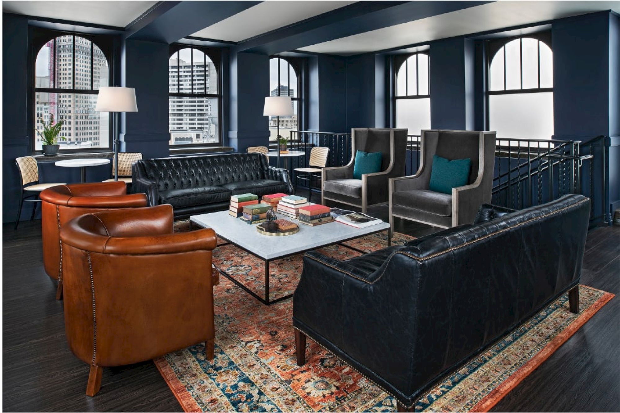 A stylish lounge area with leather sofas, armchairs, a coffee table with books, elegant lamps, and large windows.