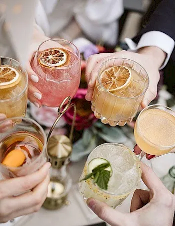 A group of people clinks glasses of refreshing cocktails and lemon drinks together in a toast, sharing a sunny moment.